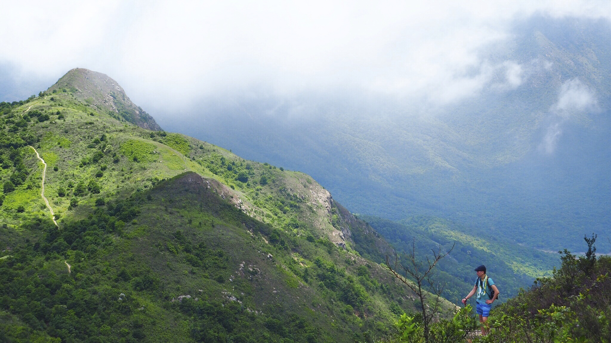 Man hiking on top of a green mountain.