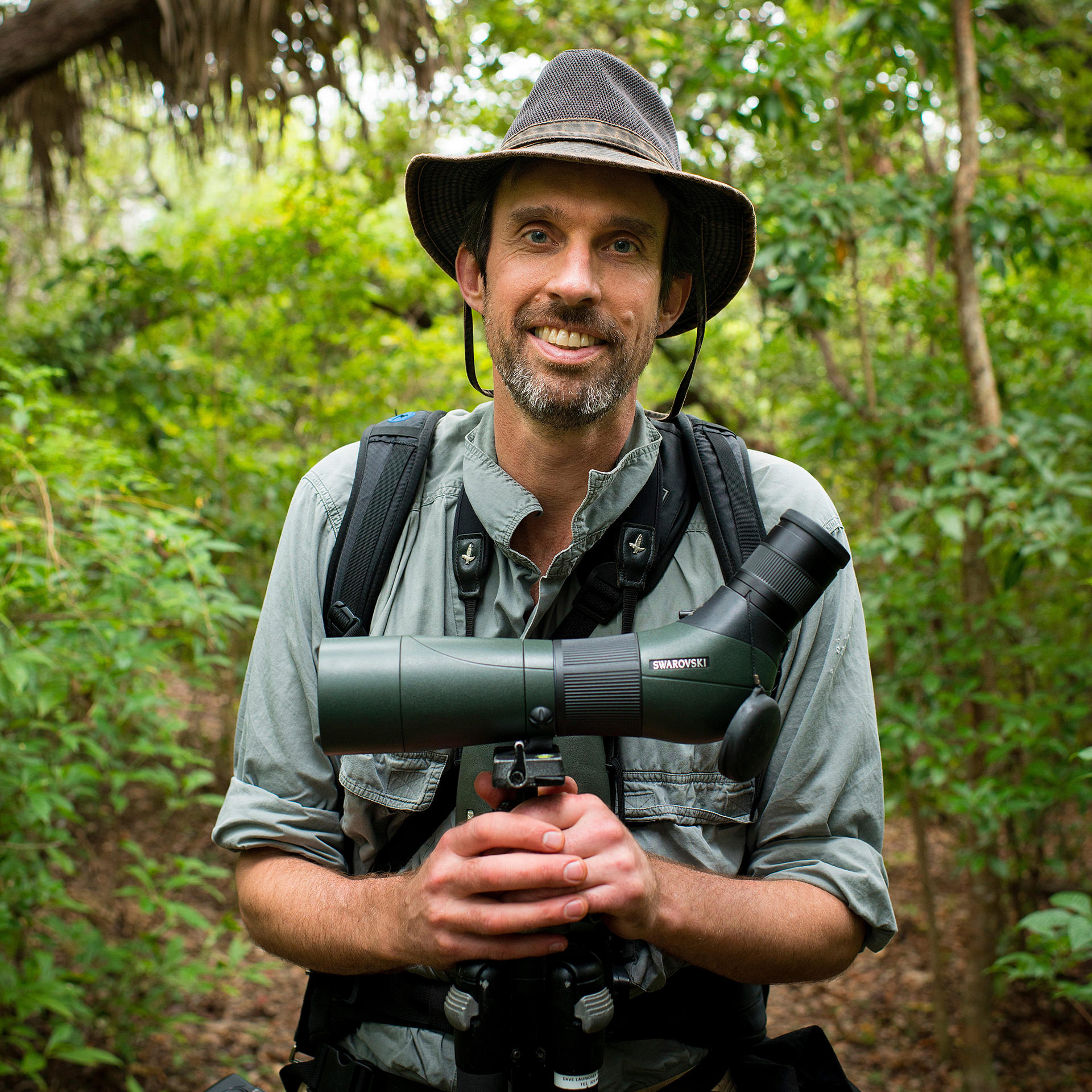 Portrait of a man standing in a forest, holding a monocular.